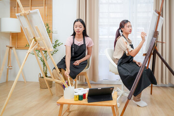 Two young asian woman artist painting on canvas. Female artist drawing with inspiration at home