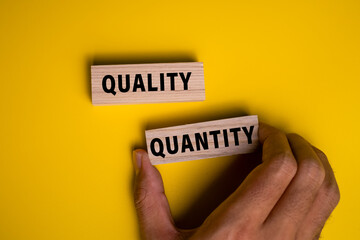 male hand holding quality and quantity words on wooden blocks isolated on yellow background