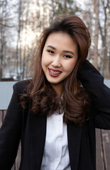 A young woman with long brown hair, wearing a black blazer and white shirt, smiles confidently...