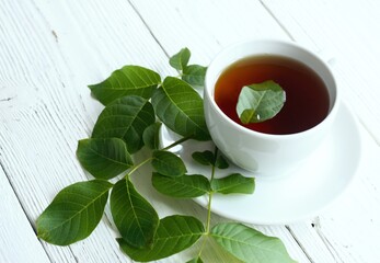 Herbal tea from fresh walnut leaves on white table.  A cup of walnut leaf infusion, traditional...