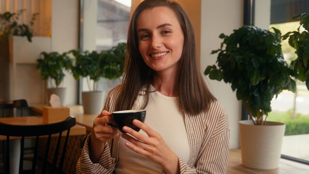 Caucasian woman sitting in cafe female girl drinking tea coffee hey you pointing gesture come here invitation looking at camera sit at table in cafeteria with croissant inviting welcome breakfast