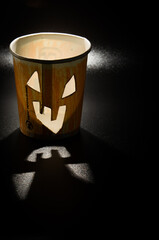 Paper cup characterized as a terrifying Halloween pumpkin with lighting inside and a black...