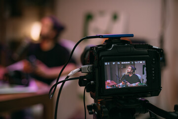 Video podcast recording studio. A young man is sitting at a table in front of a microphone in the...