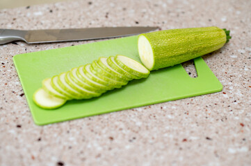 Fresh zucchini being sliced on a green cutting board in kitchen, concept: healthy cooking...
