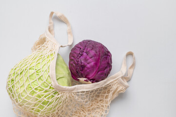 Green and purple organic cabbage in natural textile eco-friendly wicker string bag on gray...