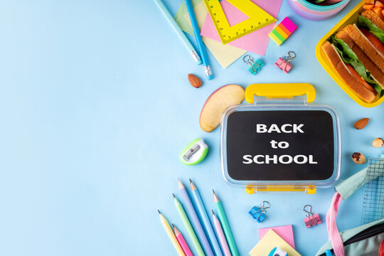 Back to school. Healthy school meal, children packed lunch box with fruit, berry, nuts, sandwich with vegetables. Kids diet snack food with education school supplies, bright blue background top view