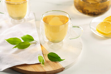 Tasty green tea in glass cups, lemon and leaves on white marble table, closeup