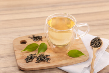 Tasty green tea in glass cup, brew and leaves on wooden table, closeup