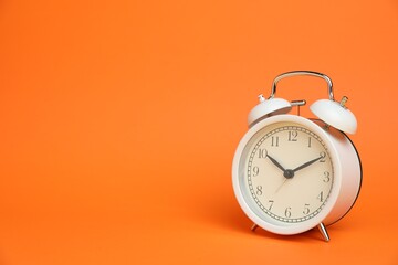 One white alarm clock on orange background, space for text