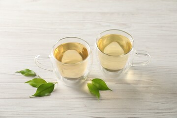 Tasty green tea in glass cups and leaves on light wooden table, above view