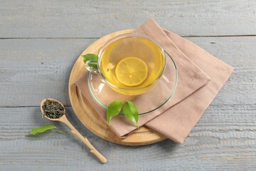 Tasty green tea with lemon in glass cup, brew and leaves on grey wooden table, above view