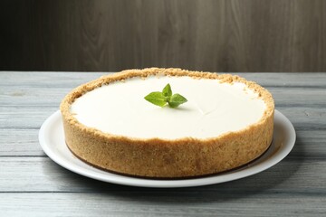 One tasty cheesecake with mint on grey table against wooden background, closeup