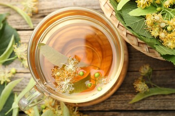 Tasty linden tea in cup, leaves and flowers on wooden table, flat lay