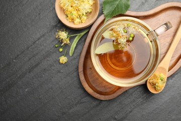 Tasty linden tea in cup, spoon, leaves and flowers on dark textured table, flat lay. Space for text