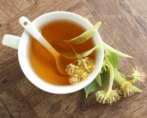 Tasty linden tea in cup, leaves and flowers on wooden table, flat lay