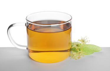 Tasty linden tea in cup, leaves and flowers on table against white background