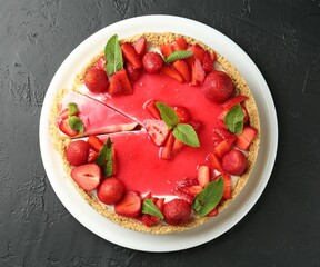 Delicious cheesecake with strawberries, sauce and mint on black table, top view