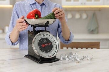 Woman weighting vegetables on kitchen scale at white marble table indoors, closeup. Space for text