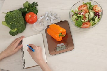 Woman developing diet plan at white wooden table with kitchen scale, healthy food and measuring...