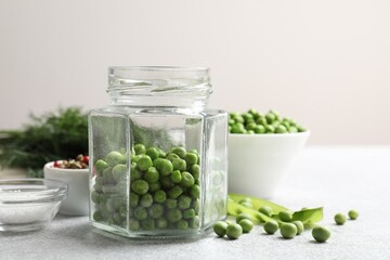 Fresh green peas in pickling jar, spices, salt and dill on white table, closeup