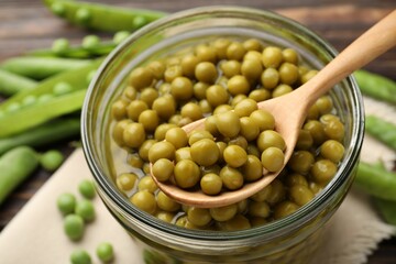 Pickled peas in jar, spoon and pods on wooden table, closeup