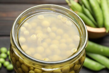 Pickled peas in jar and pods on black wooden table, closeup