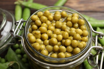 Pickled peas in jar and pods on wooden table, closeup