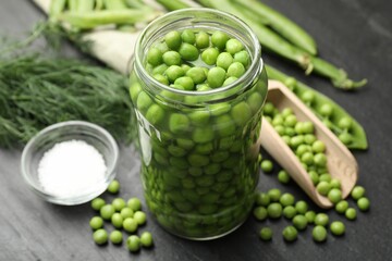 Fresh green peas in pickling jar, pods and salt on black table, closeup