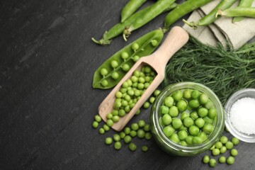 Fresh green peas in pickling jar, pods, dill and salt on black table, flat lay. Space for text