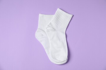 Pair of comfortable white socks on violet background, top view