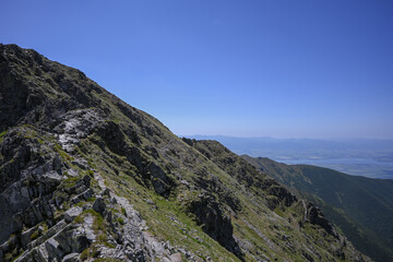 Fototapeta premium Scenic view of a hiking path ascending a steep mountain ridge, leading towards a vast valley under a clear blue sky