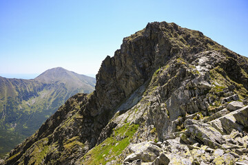Jagged rocky mountain peak overlooking a scenic valley bathed in summer sunlight