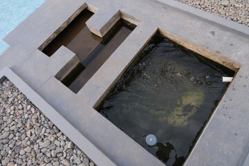 Geometric concrete fish pond featuring divided compartments with flowing water, surrounded by...
