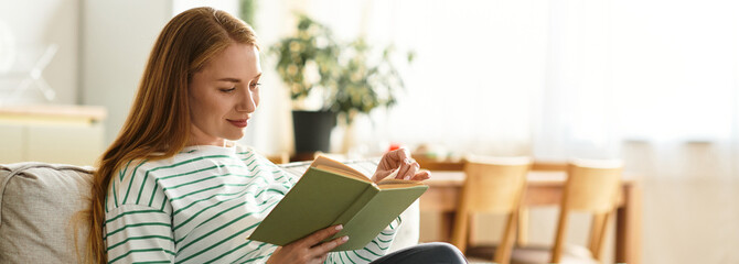 Engaging young woman enjoys a cozy reading moment at home during a sunny afternoon