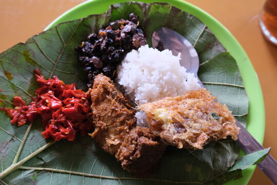 Nasi Jamblang, a Cirebonese dish served on teak leaves with rice, sambal, tempeh, egg, and seasoned side dishes on a green plate.
