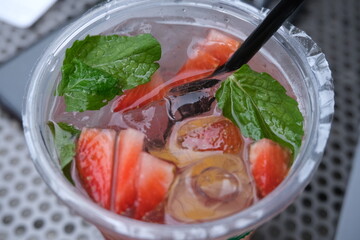 Top view of a refreshing strawberry mojito, garnished with fresh mint leaves, lime, and ice cubes in a clear plastic cup.