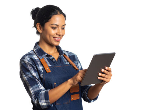 A woman in a plaid shirt and denim apron smiles while using a tablet, engaging with the device confidently and attentively.