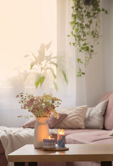 burning candles and flowers in vase in cozy living room