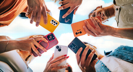 Group of young people using smart mobile phone device outside - Millenial women and men browsing on smartphone together - Trendy technology concept with guys and girls watching cellphone outdoors