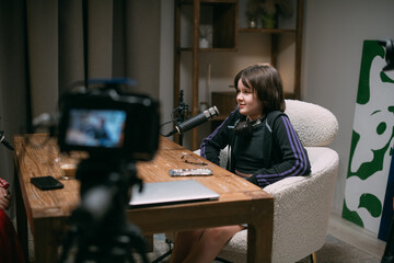 Video podcast recording studio: A conversation between a woman and a child, in front of microphones and cameras, hosted by the program's host, who interviews and releases a podcast.