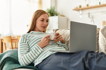Charming young woman enjoys a cozy afternoon at home while browsing on her laptop