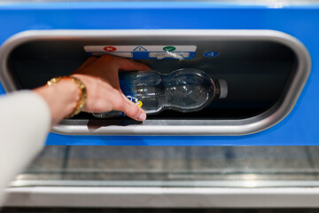 A close up of a female hand picking a water bottle from a vending machine slot. The focus is on the...