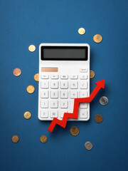A calculator with a red upward arrow on a blue background, surrounded by scattered coins, symbolizing financial growth and calculation. Top view, flat lay.