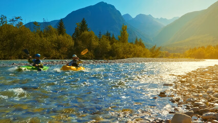 Two people, one of whom is wearing a helmet, are kayaking down a fast-flowing river surrounded by a...