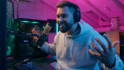 Smiling Caucasian man guy male gamer streamer playing online game at night lost upset frustrated...