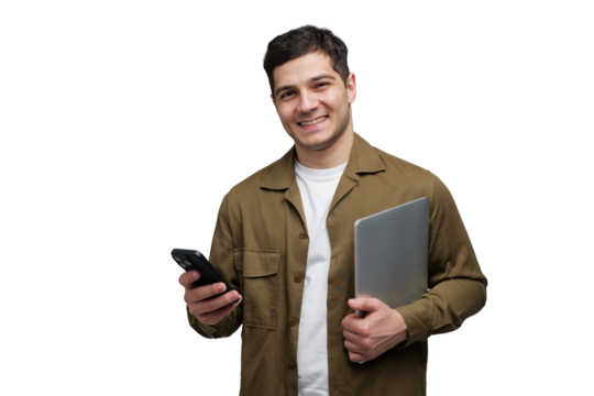 Young man smiles while holding a laptop and phone, ready for a productive day at work or school, embracing modern technology with enthusiasm