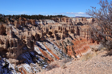 Sandy cliffs of Bryce Canyon. Daytime snapshot with clouds. There's a big dry bush ahead.