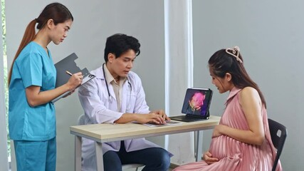 Male obstetrician, gynecologist maternal fetal medicine specialist examines pregnant woman ultrasound results looks at laptop with interest and discusses with female nurse assistant recording results.