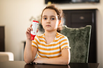 Cute little girl monitoring peak expiratory with peak flow meter at home. Hand medical device used...