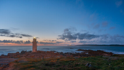 Twilight over Muxía lighthouse Galicia Spain beacon lit on rocky coast facing Atlantic calm waves under fading sky peaceful maritime landscape solitude guidance resilience